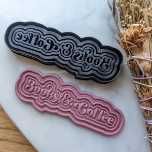May include: Two cookie cutters, one black and one pink, with the words "Books & Coffee" in a retro font.
