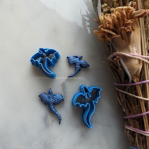 Puede incluir: Cuatro cortadores de galletas de plástico azul con forma de dragones. Los cortadores están sobre una superficie de mármol blanco.