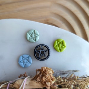 May include: Four small pentagram-shaped charms, one black, one light green, one light blue, and one light green. The charms are on a white surface.