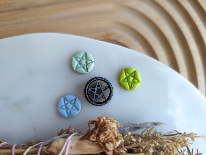 May include: Four small pentagram-shaped charms, one black, one light green, one light blue, and one light green. The charms are on a white surface.
