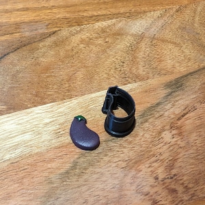 May include: A purple eggplant-shaped cookie cutter and a small purple eggplant-shaped cookie on a wooden surface.