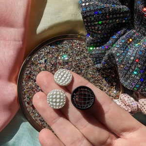 May include: Three round buttons, two white and one black. The white buttons have a textured surface. The black button has a grid pattern.