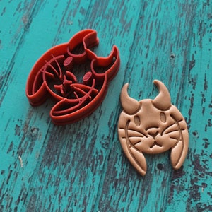 Puede incluir: Un cortador de galletas de plástico rojo con forma de conejo con cuernos y una galleta marrón cortada con el cortador.