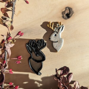 Puede incluir: Dos cortadores de galletas de reno negros y plateados sobre una superficie de madera con una rama seca con bayas rojas.