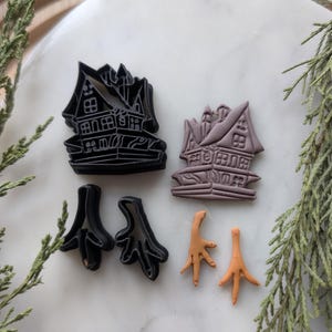 May include: A set of five cookie cutters, including two haunted houses and two sets of chicken feet. The haunted houses are black and the chicken feet are orange.