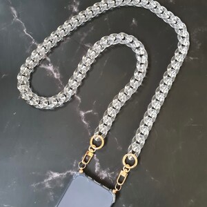 May include: A clear plastic chain phone strap with gold clasps. The strap is made of thick, chunky links and is designed to be worn around the neck.