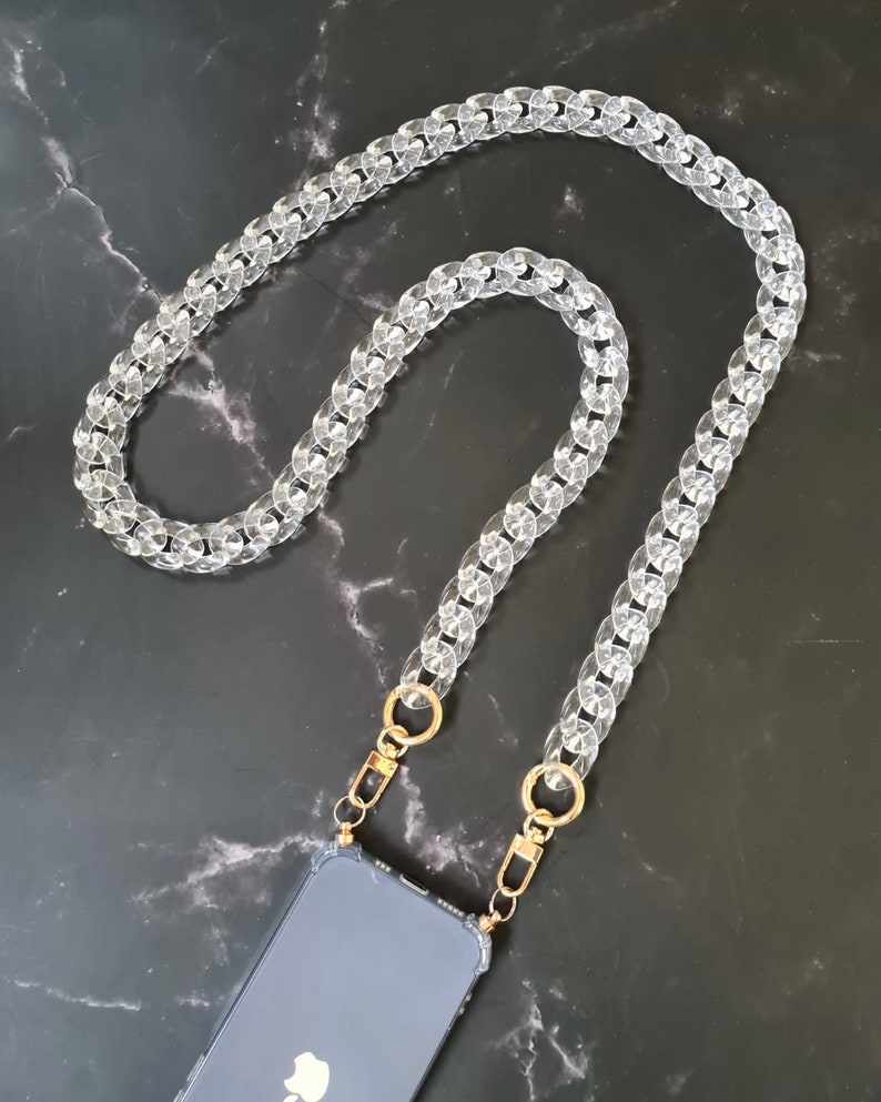 May include: A clear plastic chain phone strap with gold clasps. The strap is made of thick, chunky links and is designed to be worn around the neck.
