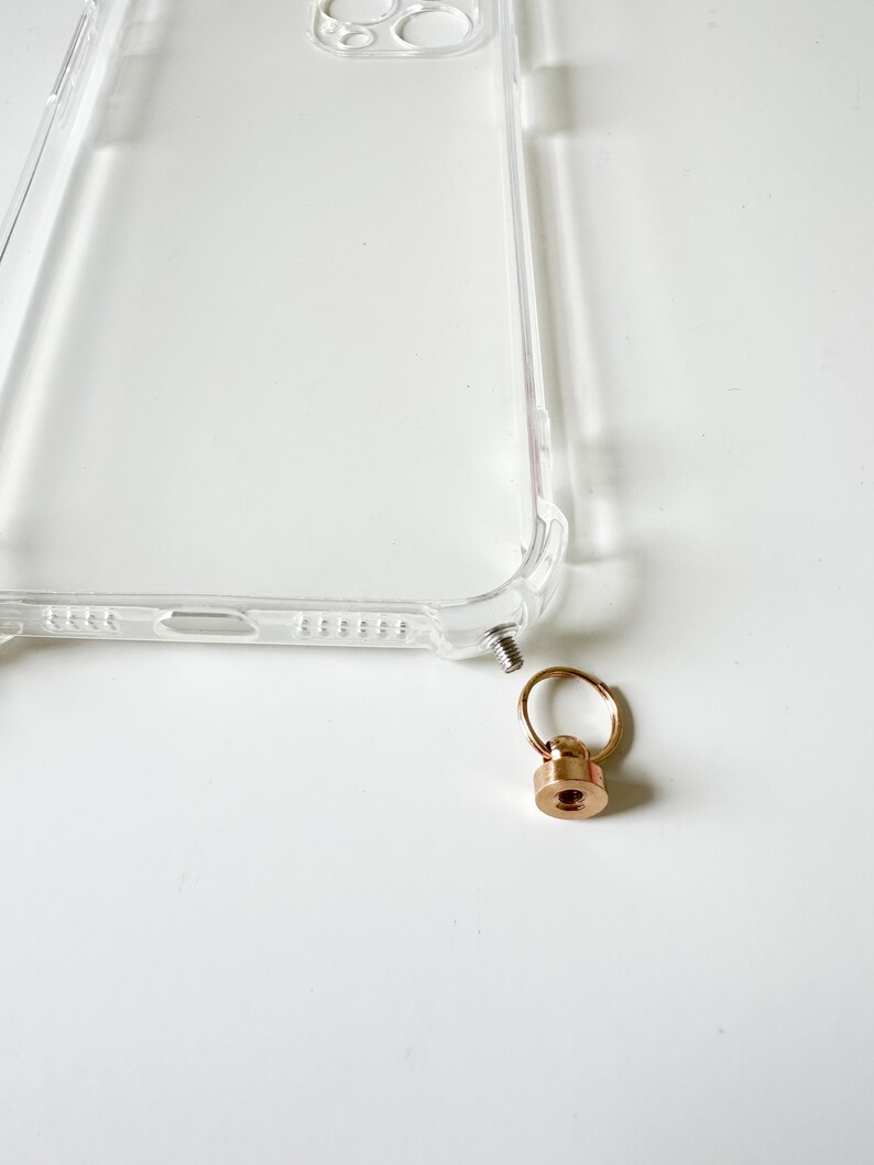 May include: A clear phone case with a gold metal ring and screw attachment.