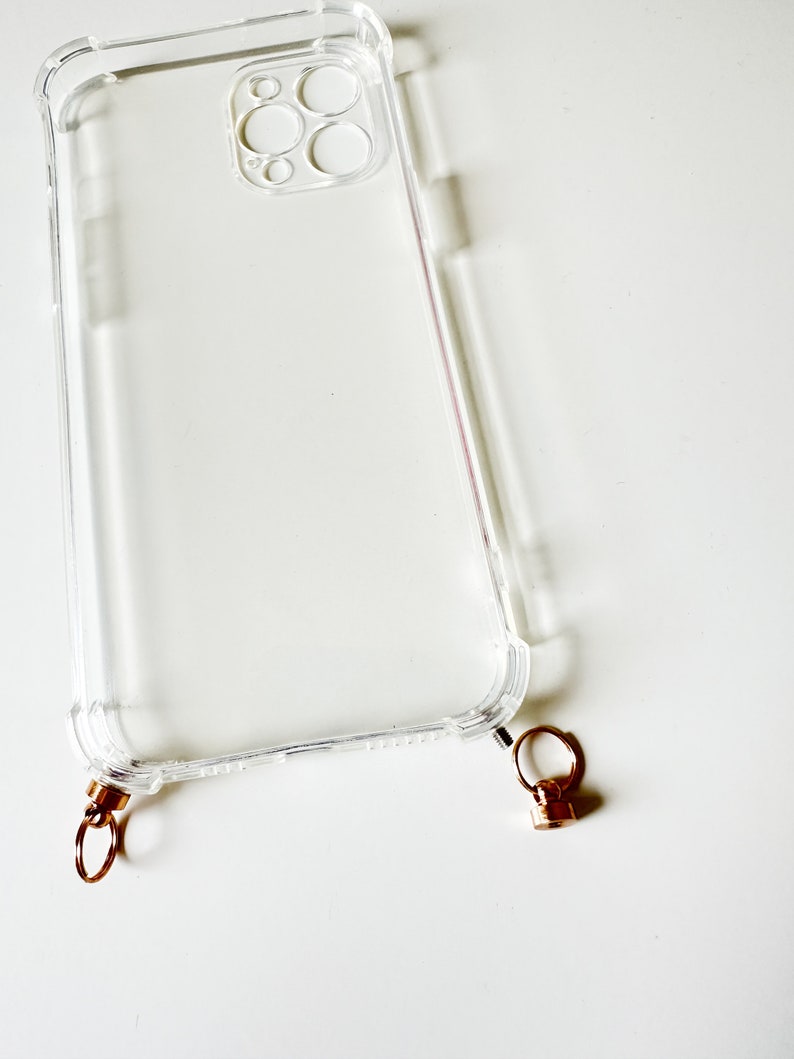 May include: A clear plastic phone case with a gold metal ring attached to the bottom. The case has a raised lip around the camera lens.