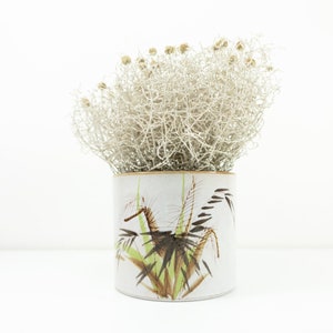 Könnte beinhalten: Ein weißer Keramiktopf mit braunem und grünem Blumendesign. Der Topf ist mit getrockneten weißen Blumen gefüllt.