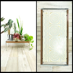 May include: A mid-century modern glass top coffee table with a white and gray geometric pattern. The table has a chrome frame and is sitting on a light wood floor.