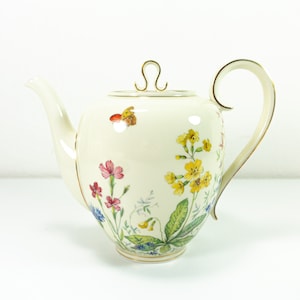 Könnte beinhalten: Eine weiße Porzellan-Teekanne mit einem Blumendesign mit rosa, gelben und blauen Blumen, grünen Blättern und einem Schmetterling. Die Teekanne hat einen goldenen Rand und einen goldenen Henkel.