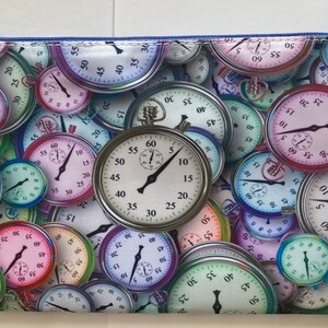 May include: A rectangular zippered pouch featuring a repeating pattern of colorful stopwatches and clocks. The design includes various colors like pink, green, blue, and purple. The zipper is blue.