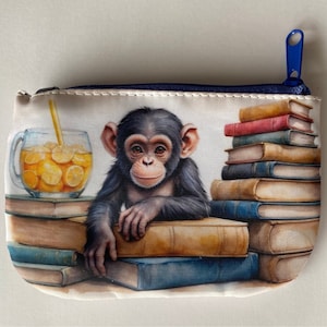 May include: A blue zippered pouch with a whimsical illustration of a chimpanzee sitting on a stack of books. The chimpanzee is holding a glass of lemonade with a straw. The pouch is perfect for storing small items like coins, keys, or makeup.