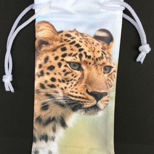May include: White drawstring bag with a leopard print design. The leopard is looking to the right with its head tilted slightly. The bag is made of a soft, white fabric.