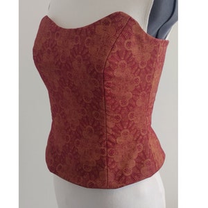 May include: A strapless red and gold corset with a floral pattern. The corset is made of a soft, silky fabric and has a boned structure.