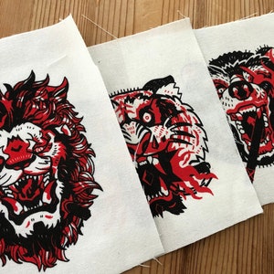 May include: Three fabric patches with black and white illustrations of a lion, tiger, and bear with red flames. The animals are depicted with open mouths and sharp teeth.
