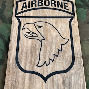 May include: A wooden sign with a black outline of an eagle head and the word "AIRBORNE" in a black banner above the eagle.