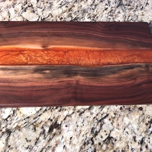 May include: A rectangular walnut wood cutting board with a thick orange resin inlay. The board has a natural wood finish and is perfect for serving cheese, charcuterie, or other appetizers.