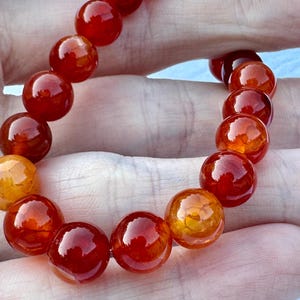 May include: A red and orange agate gemstone bracelet with round beads. The bracelet is made of natural stones and has a polished finish.