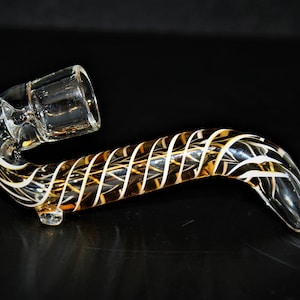 May include: A glass pipe with a clear bowl and a brown and white swirl design.