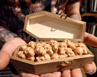 May include: A wooden coffin-shaped box filled with small, light brown skull-shaped candies. The box is open and the candies are visible inside.