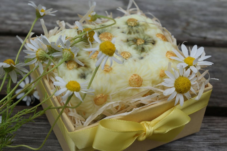 May include: A yellow gift box with a white and gold floral design, tied with a yellow ribbon, and filled with white daisies.
