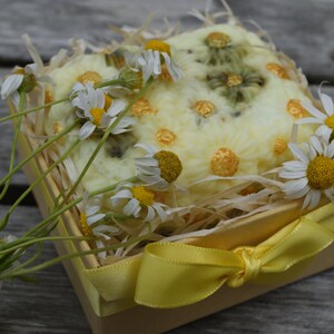 May include: A yellow gift box with a yellow ribbon tied in a bow. The box is filled with a white crocheted soap bar decorated with yellow dots and dried chamomile flowers.