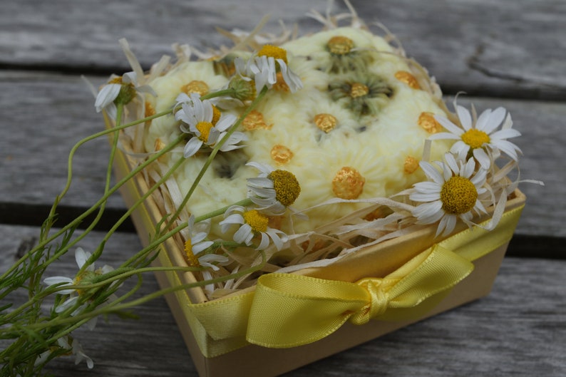 May include: A yellow gift box with a yellow ribbon tied in a bow. The box is filled with a white crocheted soap bar decorated with yellow dots and dried chamomile flowers.
