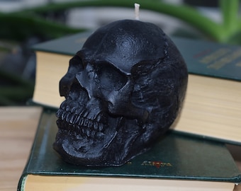 May include: A black skull-shaped candle with a white wick. The candle is sitting on top of a stack of books.