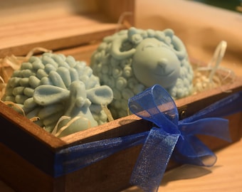 May include: Two blue sheep-shaped soaps in a wooden box with a blue ribbon. The box is filled with shredded paper.