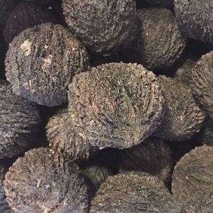 以下が含まれることがあります： 暗褐色のテクスチャード加工されたクルミの山をクローズアップ。クルミはざらざらしたでこぼこの表面をしており、ぎっしりと詰まっています。色は濃いアースカラーの茶色です。