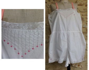 May include: White cotton slip with pink embroidery and lace trim. The slip has a sleeveless design and a fitted bodice.