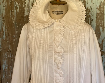 May include: A white cotton blouse with a large, lace-trimmed collar and a ruffled front. The blouse has a fitted bodice and long sleeves with lace cuffs.