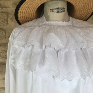 Op de afbeelding: Witte katoenen blouse met een kantversiering en een gerimpelde halslijn. De blouse heeft een vintage look en is perfect voor een zomerdag.
