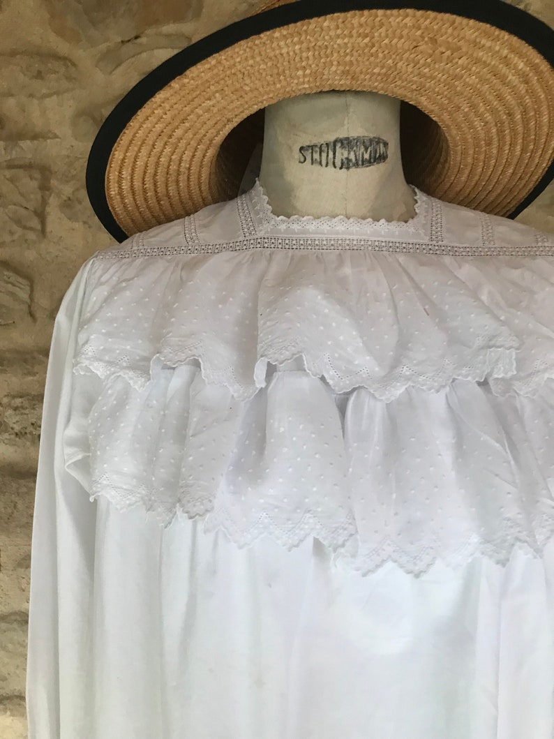 Op de afbeelding: Witte katoenen blouse met een kantversiering en een gerimpelde halslijn. De blouse heeft een vintage look en is perfect voor een zomerdag.