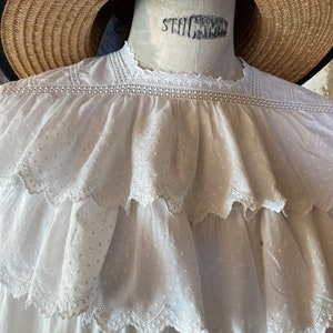 Op de afbeelding: Witte katoenen blouse met een gerimpelde halslijn en een gestippeld patroon. De blouse heeft een delicate kantversiering rond de halslijn en de ruches.