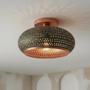 May include: A bronze-colored, semi-flush mount ceiling light fixture. The fixture has a perforated, dome-shaped shade with a copper-colored interior and a copper-colored base. The light is on, casting a warm glow.