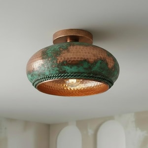 May include: A copper ceiling light fixture with a hammered texture and a verdigris finish. The light has a round, bowl-shaped shade with a rope-like trim and a warm, inviting glow.