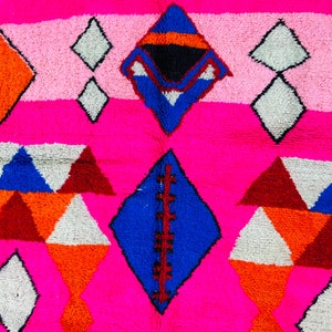 May include: A pink, white, blue, orange, and red geometric patterned rug with a diamond shape in the center.