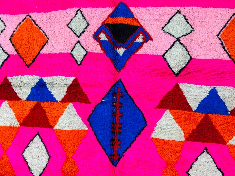 May include: A pink, white, blue, orange, and red geometric patterned rug with a diamond shape in the center.