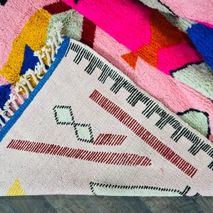 May include: A pink, blue, yellow, and red geometric patterned rug with fringe. The rug has a white background with a black diamond pattern.