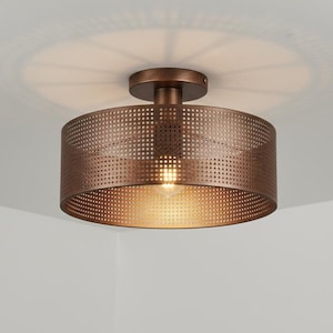 May include: A bronze-colored, drum-shaped ceiling light fixture. The light has a perforated shade and a single bulb. The fixture is mounted on a white ceiling. The light casts a circular shadow.