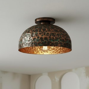 May include: A bronze-colored, dome-shaped ceiling light fixture. The hammered metal shade has a textured surface with green and brown hues. The interior is gold, and a single light bulb is visible.
