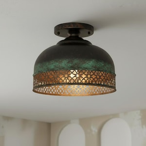 May include: A ceiling light with a bronze finish. The dome-shaped shade has a dark brown top, a green-blue patina, and a decorative, openwork bronze band. The light is mounted on a circular base. The light fixture is a decorative element.