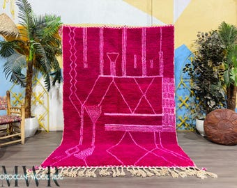 May include: A pink Moroccan wool rug with a geometric pattern in white. The rug has a fringe border and is displayed on a wooden floor.