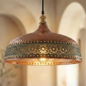 May include: A dome-shaped pendant light fixture featuring a hammered copper finish on the upper section and a wide, dark green band with intricate, laser-cut geometric star patterns. A brass-toned socket connects to a black cord at the top.