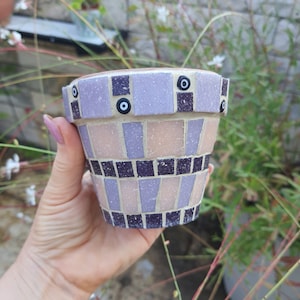 Pode incluir: Um pequeno vaso de flores de mosaico roxo e rosa com amuletos de olho turco preto e branco. O vaso é feito de cerâmica e tem uma forma redonda.