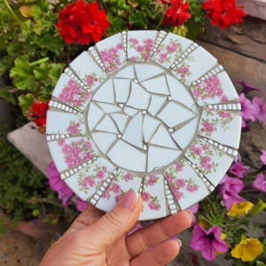 Puede incluir: Un azulejo de mosaico de cerámica blanca con un patrón floral. El azulejo está hecho de pequeñas piezas irregulares de cerámica que están dispuestas en un patrón circular. El patrón floral es rosa y blanco y presenta pequeñas flores y hojas. El azulejo es perfecto para agregar un toque de elegancia a cualquier proyecto de decoración del hogar.