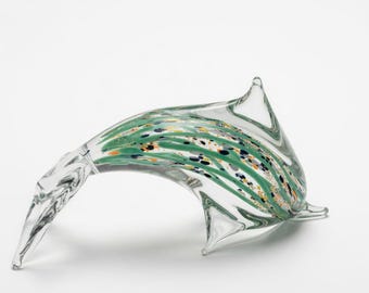 May include: A clear glass dolphin sculpture with green, yellow, and black decorative streaks. The dolphin has a curved body and pointed fins. The sculpture is displayed on a white background.